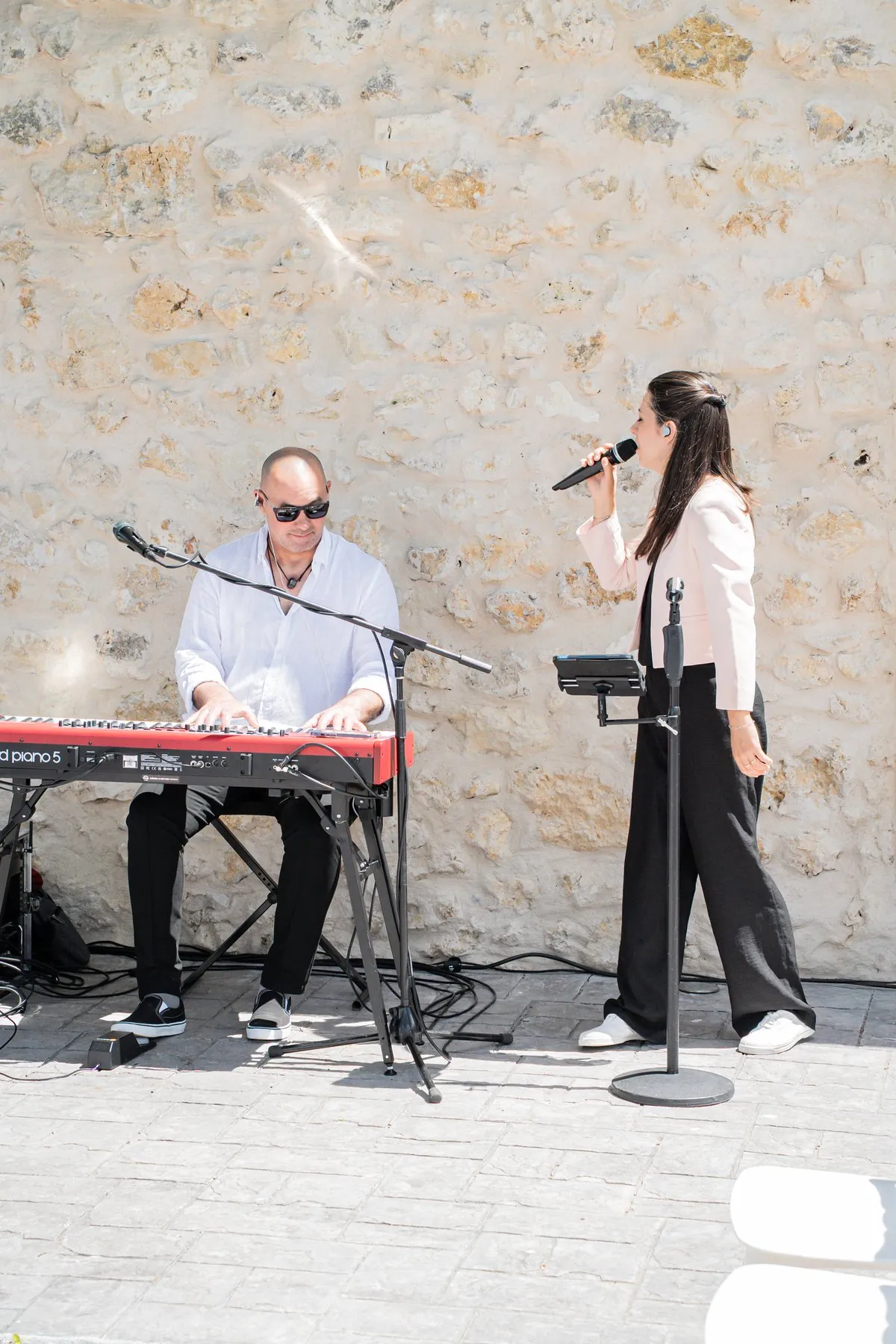 Le duo Mahkah en live : Stéphane au piano Nord et Mathilde au chant, devant un mur de pierre en extérieur