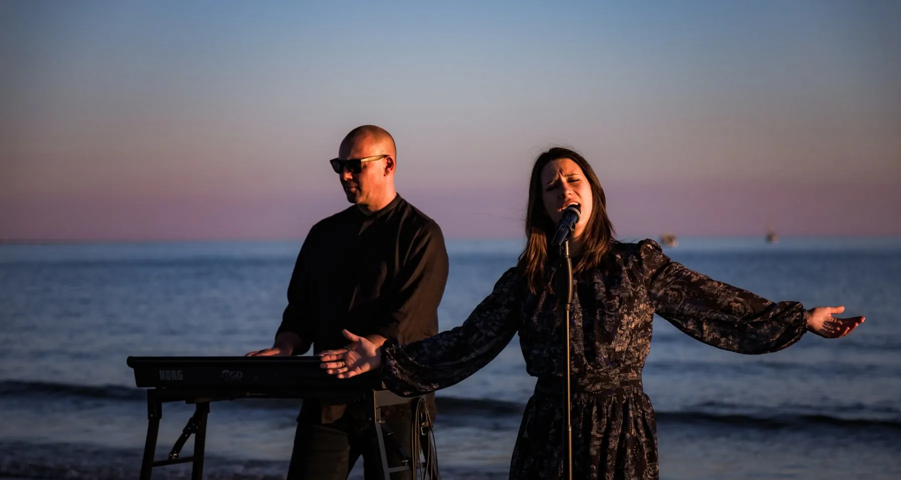 Le duo Mahkah en live au coucher du soleil au bord de la mer : Stéphane au piano et Mathilde au chant, bras ouverts
